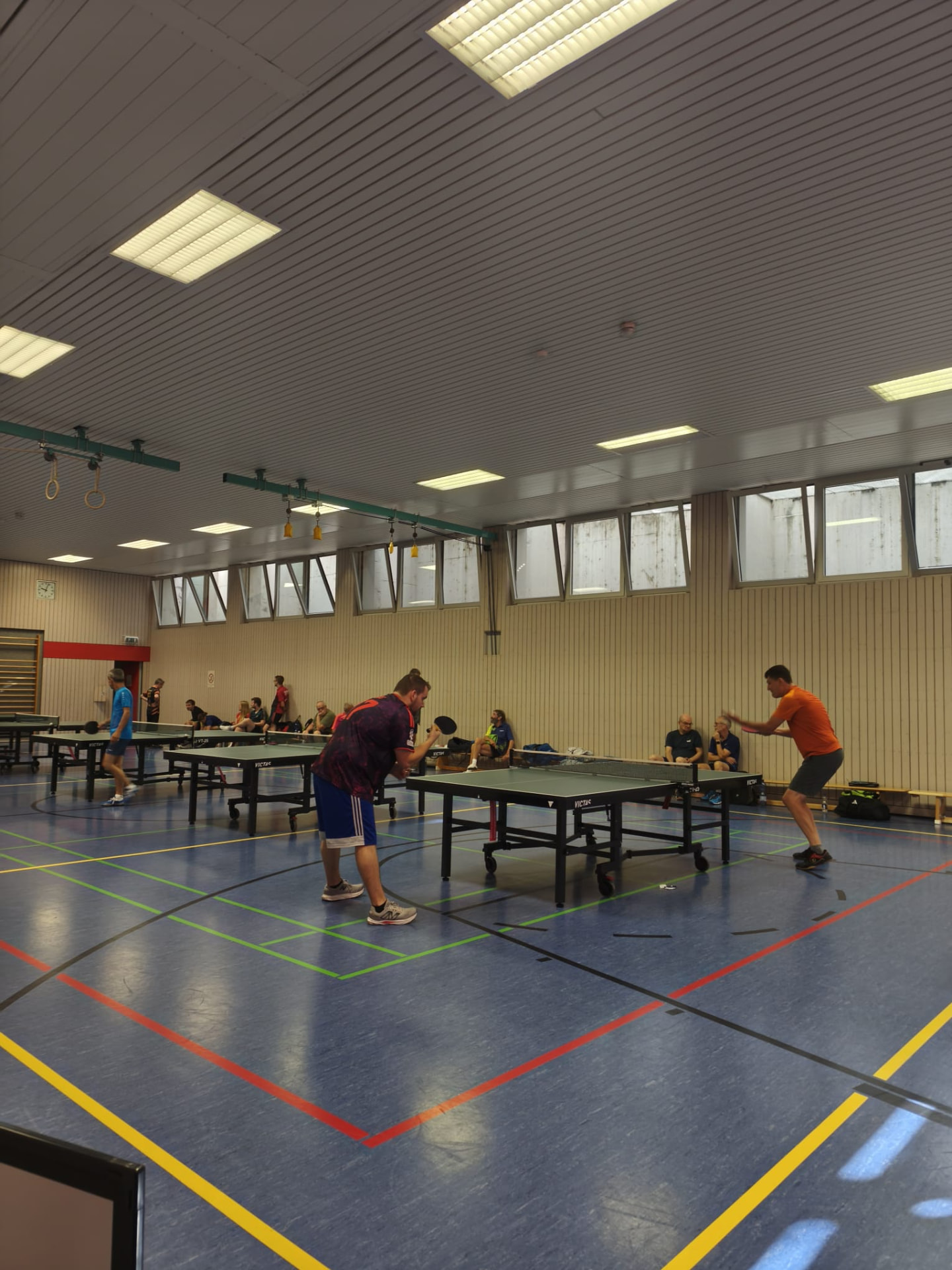 Zwei Spieler beim Trainingsspiel in der Halle, weitere Spieler an den Tischen